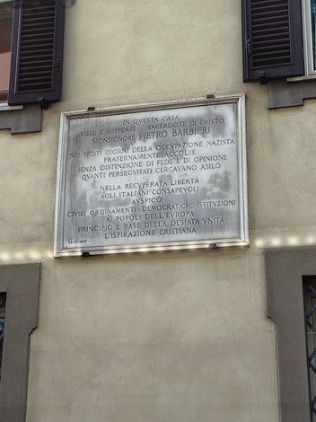 Lapide commemorativa dedicata a Monsignor Pietro Barbieri, situata su una facciata di edificio storico.