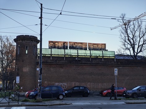 Pannelli affissi sul carcere Le Nuove, con volti di imprigionati visibili sopra il muro.