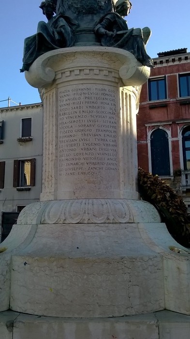 Monumento ai caduti dei Carmini, con iscrizioni commemorative e statue sullo sfondo di edifici storici.