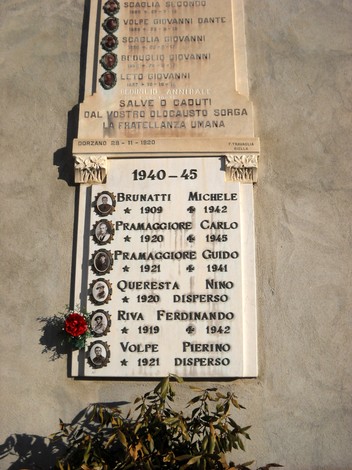 Lapide commemorativa dedicata ai caduti della Seconda Guerra Mondiale, con nomi e date. Fiore rosso in omaggio.