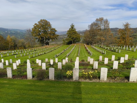 Cimitero di guerra sudafricano, con lapidi bianche immerse nel verde e in una cornice di alberi e colline.