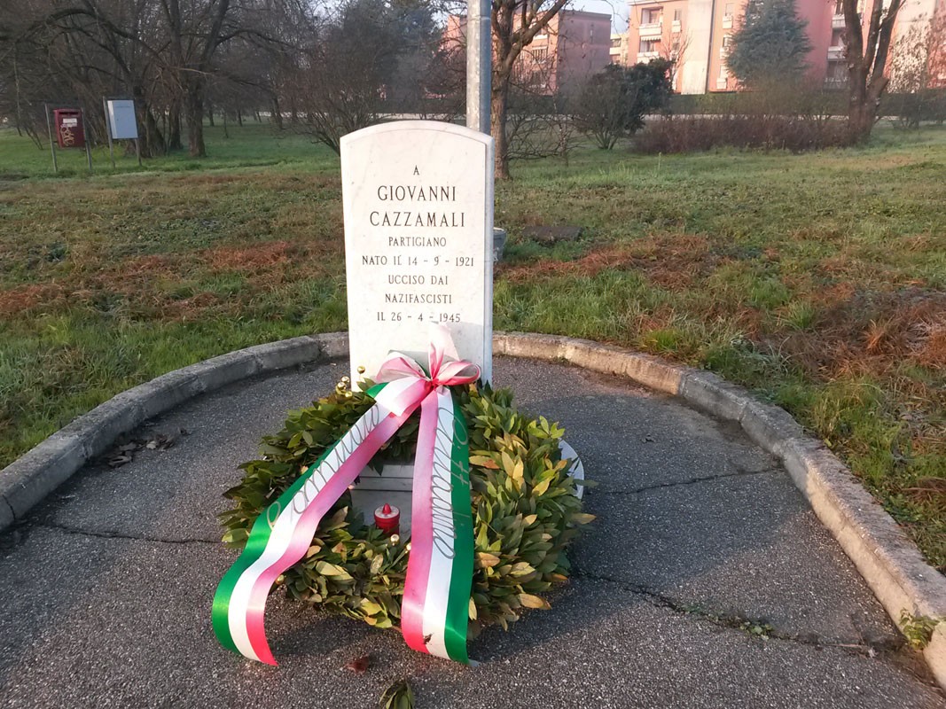 Cippo commemorativo dedicato a Giovanni Cazzamali, partigiano ucciso dai nazifascisti. Di fronte a un paesaggio verde.