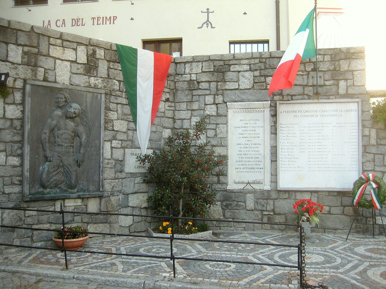 Lapidi commemorative ai caduti di Traversella, con bandiere italiane e monumento in pietra.