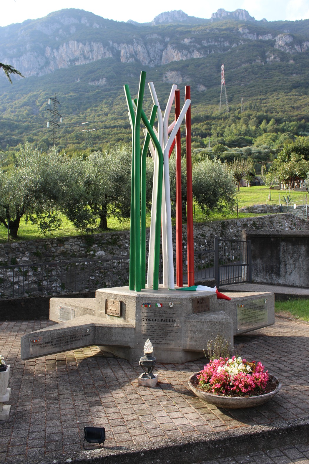 Monumento ai caduti partigiani, con colonne di metallo colorate in bianco, rosso e verde, immerso nel verde.