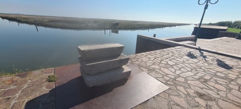 Monumento a Isepetto, tre massi sovrapposti, vista sul fiume con riva e paesaggio naturale circostante.