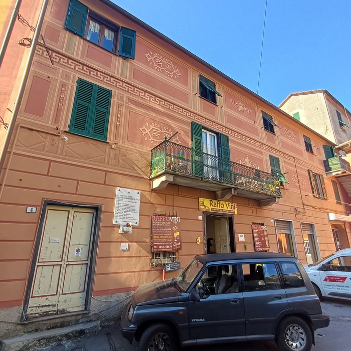 Facciata di un palazzo con targa e lapide accanto al portone, insegna "Raffo Vini" al piano terra.