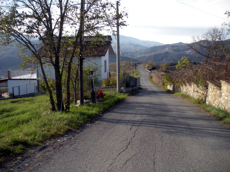 Panorama di Canevari con strada asfaltata, case rurali e vegetazione che si estende verso le colline circostanti.