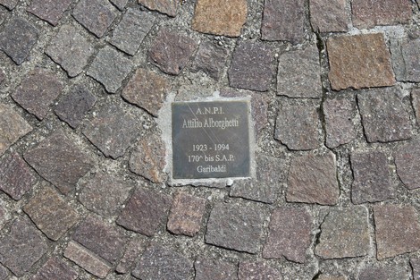 Pietra d'inciampo dedicata ai partigiani, incastonata in un pavimento di ciottoli.