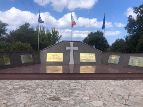 Sacrario dei caduti di Cefalonia, monumento commemorativo con croce e bandiere, immerso nella natura.