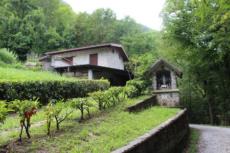 Lapide commemorativa dedicata ai caduti per la libertà, immersa nel verde di Vertova, vicino a un edificio di pietra.