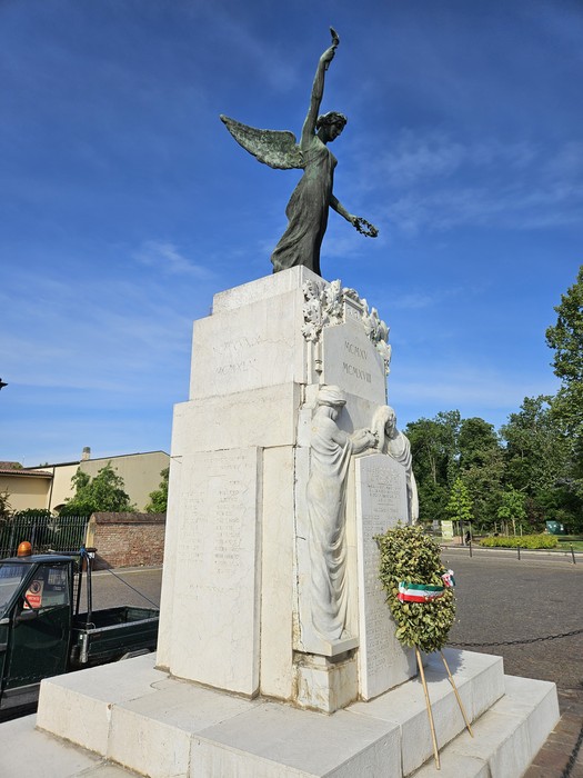 Monumento ai Caduti di San Giovanni in Croce, con statue e decorazioni, immerso in un contesto verde.