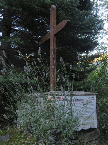 Croce di legno circondata da piante e arbusti, in un ambiente naturale e sereno.