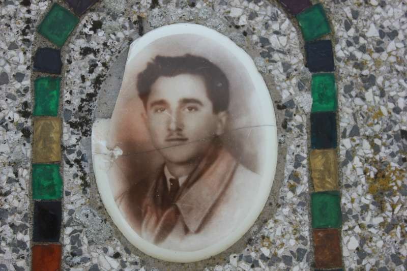 Cippo commemorativo decorato con una fotografia in ceramica di un uomo in posa formale.