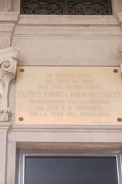 Lapide in marmo con iscrizione, murata sulla facciata di un edificio tra due capitelli decorati.