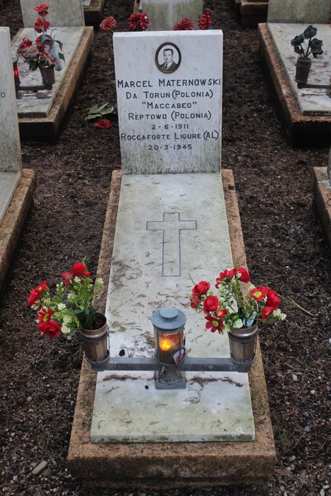 Tombe di caduti per la Libertà con decorazioni floreali e lumini commemorativi in un cimitero.