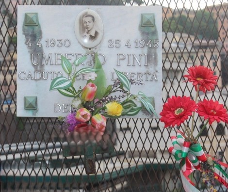 Lapide commemorativa di Umberto Pini con fiori, ubicata in un contesto urbano.