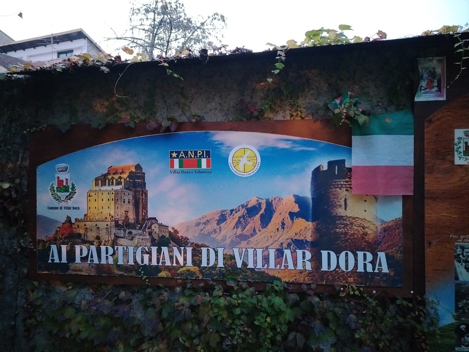 Giardino memoriale a Blandino con pannello commemorativo dedicato ai partigiani di Villar Dora, circondato da natura.