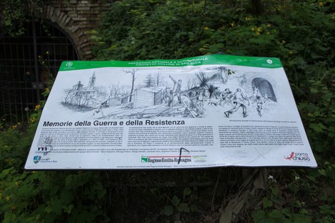 Scorcio del "Sentiero dei Bregoli" con pannello informativo su memorie di guerra e resistenza, immerso nella vegetazione.