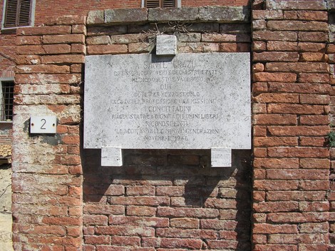 Lapide commemorativa dedicata a Grazi, in pietra su muro di mattoni rossi.