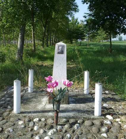 Cippo commemorativo con fiori, immerso in un ambiente naturale e tranquillo.