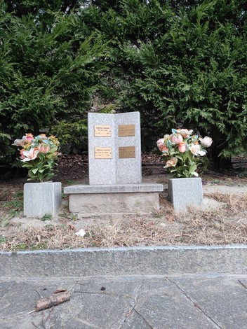 Monumento nel Parco della Rimembranza, circondato da vegetazione e fiori artificiali in un contesto tranquillo.