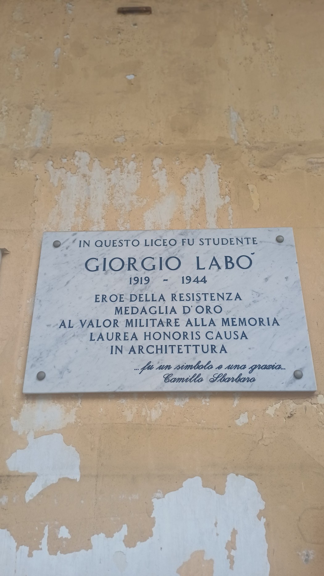 Lapide marmorea con iscrizione, fissata su una parete esterna intonacata.