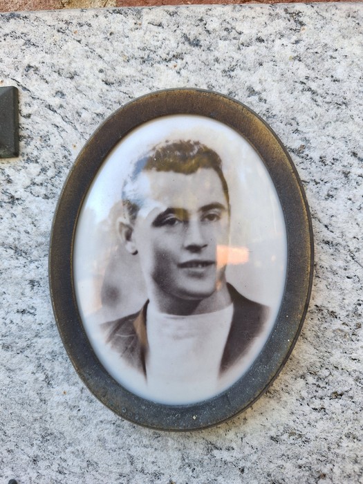 Ritratto ovale in cornice bronzea di un giovane uomo, applicato su una parete in pietra.