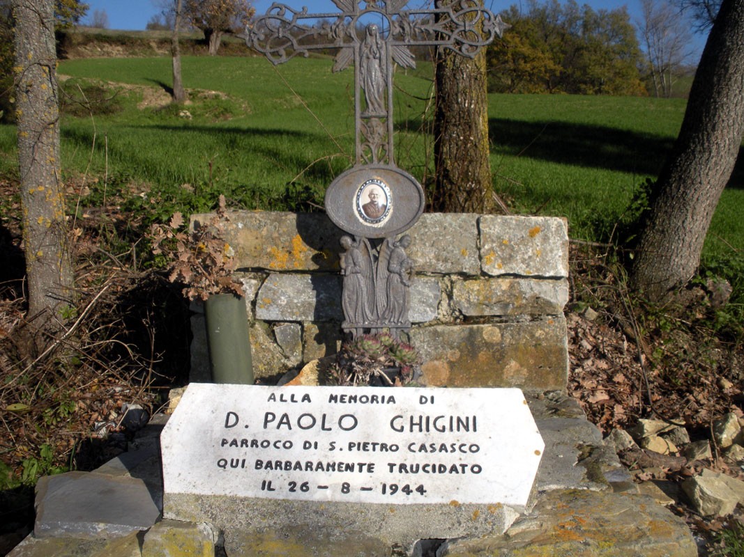 Croce commemorativa dedicata a D. Paolo Ghigini, parroco trucidato nel 1944, situata in un paesaggio verde.