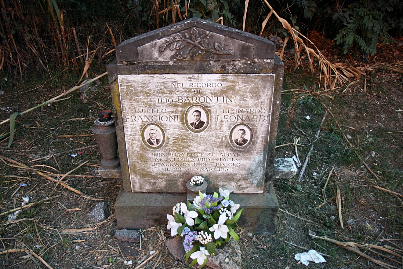 Cippo commemorativo dedicato a Barontini, Frangioni e Leonardi, circondato da fiori e vegetazione.