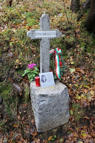 Croce commemorativa di Gervasoni, con fiori e una dedica, immersa nella natura autunnale.