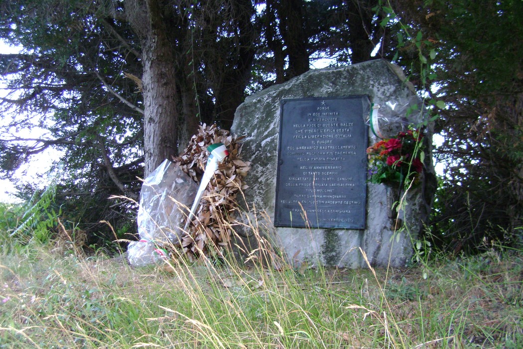 Cippo commemorativo della Brigata Muccini, con decorazioni floreali, immerso nella natura.
