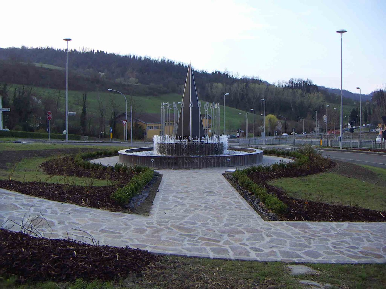 Monumento a D'Acquisto, situato in un'area verde con fontane, circondato da un percorso in pietra.