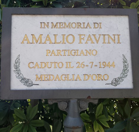 Lapide commemorativa di Amalio Favini, partigiano caduto nel 1944, con decorazioni artistiche e scritte dorate.