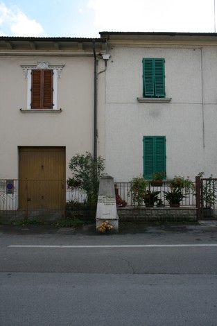 Cippo commemorativo a Brocherel, con case e fiori, rappresenta la memoria storica del luogo.