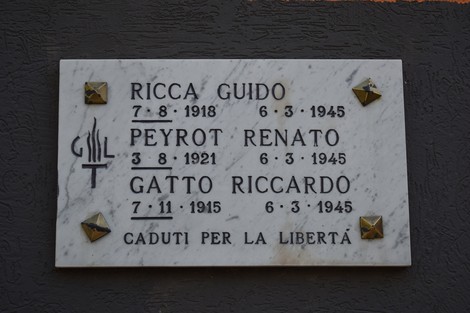Lapide commemorativa in marmo con nomi di tre individui caduti per la libertà, decorata con simboli metallici.