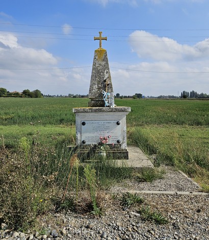 Cippo commemorativo ai Martiri di Bondanello, circondato da campi verdi e cielo nuvoloso.