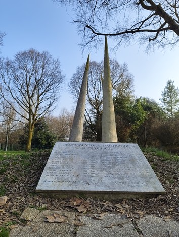 Monumento ai partigiani di Argelato con obelischi e iscrizioni, immerso nella natura.