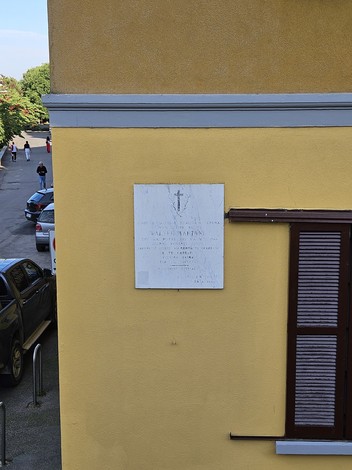 Lapide commemorativa affissa su un muro giallo, situata a Martani, con dettagli storici e decorativi.