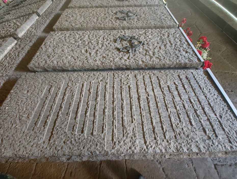 Interno del Mausoleo delle Fosse Ardeatine, con tombe in pietra decorate e fiori commemorativi.