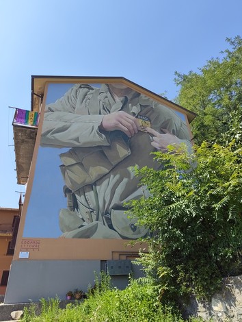 Murale su parete di edificio, raffigura un soldato con divisa militare e iscrizione alla base.