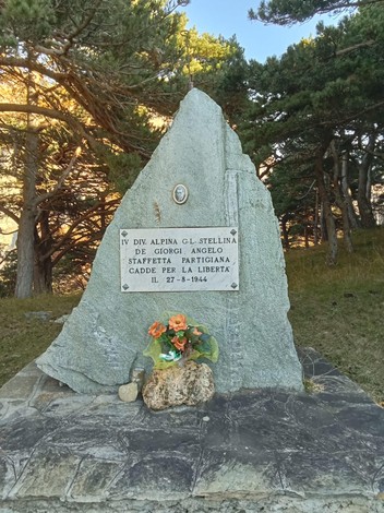 Monumento a De Giorgi, dedicato al partigiano caduto per la libertà, circondato da alberi e fiori.