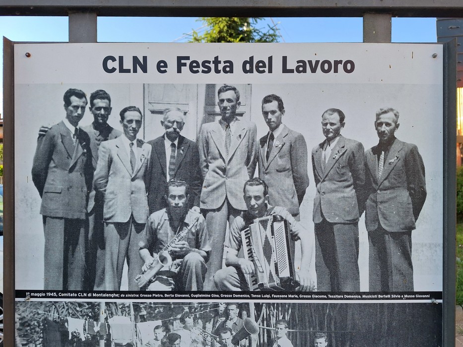 Pannello all'aperto con foto storica in bianco e nero di un gruppo di uomini e didascalia con titolo e iscrizione.