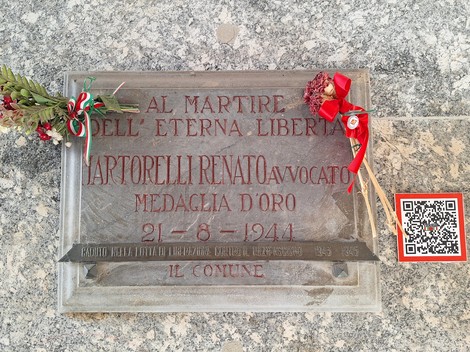 Lapide commemorativa dedicata a Renato Martorelli, con decorazioni floreali e simboli celebrativi.