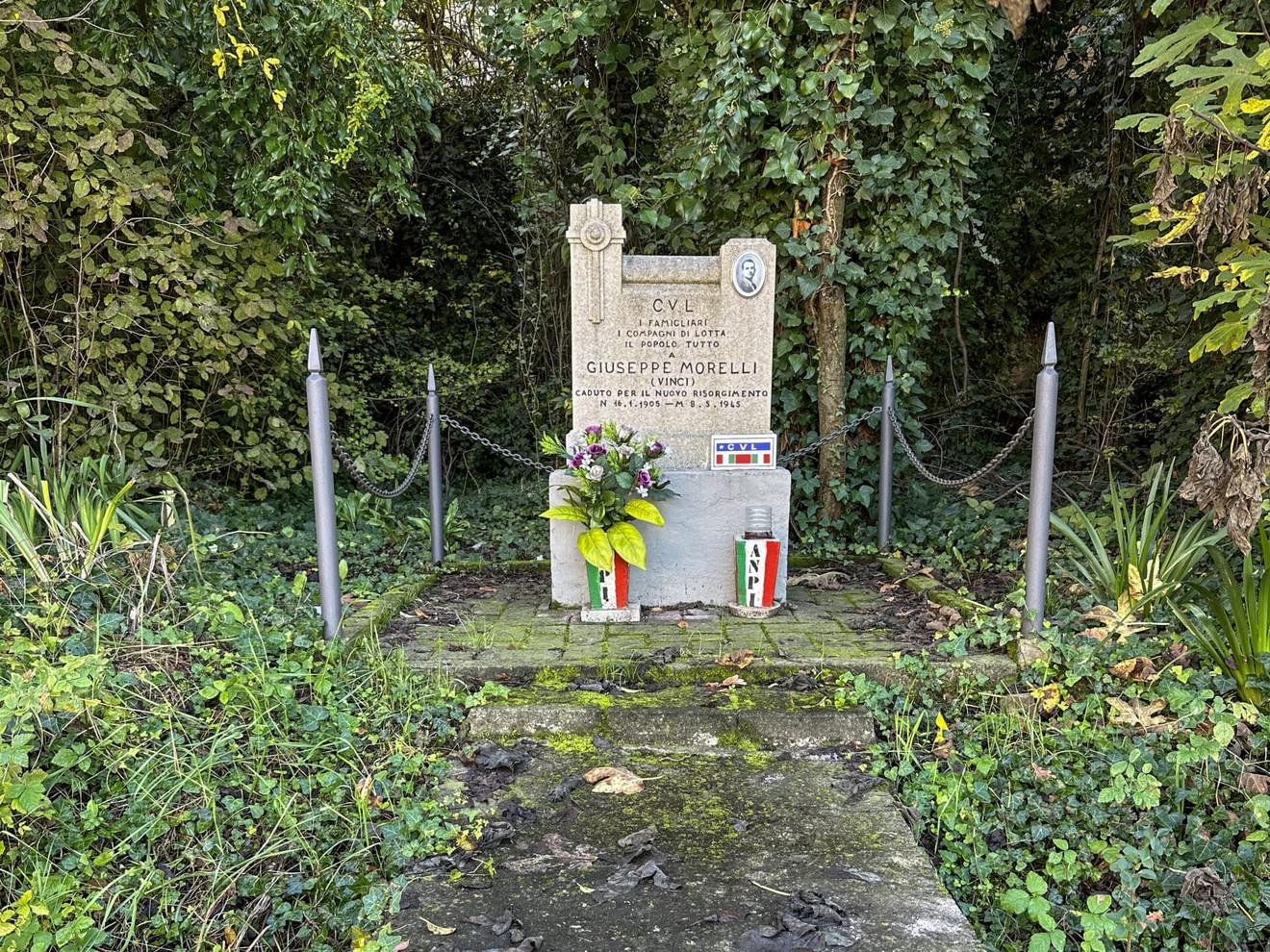 Cippo commemorativo dedicato a Giuseppe Morelli, circondato da vegetazione.