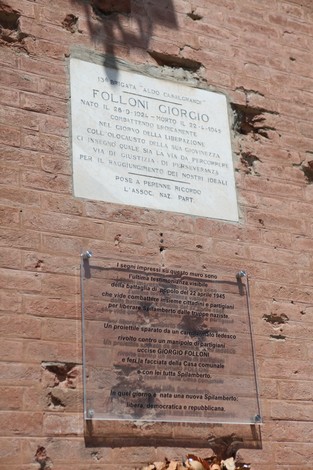 Lapide commemorativa e targa in onore di Giorgio Folloni, situata in un muro di mattoni.