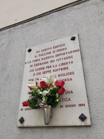 Lapide commemorativa per i deportati in Germania, con un omaggio floreale in memoria delle vittime.