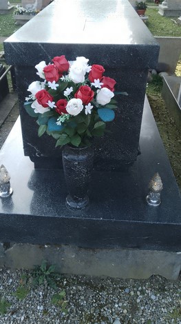 Tomba di Di Vona con fiori artificiali, caratterizzata da un vaso di rose rosse e bianche. Ambiente cimiteriale.