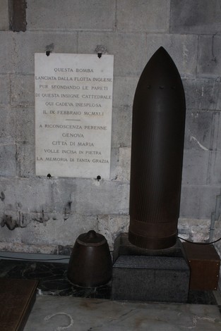 Lapide commemorativa accanto a una bomba inesplosa, segno di un evento storico, in un contesto di memoria e riflessione.