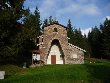 Il Tempio ai Dodici Martiri è una costruzione in pietra immersa nel verde, circondato da alberi e cielo sereno.