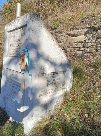 Monumento ai caduti per la Libertà, con iscrizioni commemorative e decorazioni floreali in un contesto naturale.